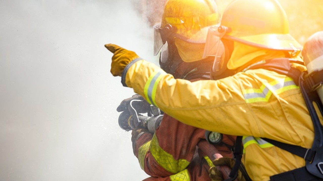 2 fireman in full gear, pointing at something in the distance